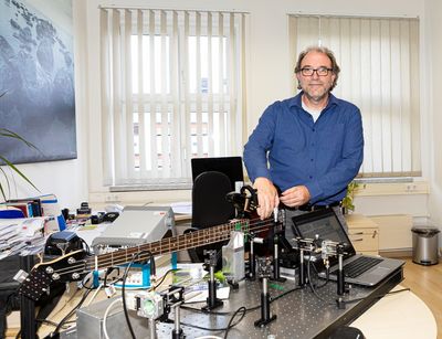 Prof. Dr. Jan Meijer mit einem roten Diamanten und einer E-Gitarre und dem Versuchsaufbau