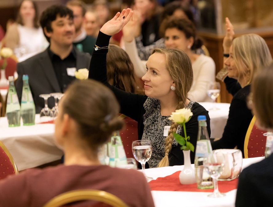 zur Vergrößerungsansicht des Bildes: Teilnehmende im Publikum heben die Hand