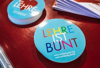 Zwei Stapel Aufkleber mit Schriftzügen in bunten Lettern: „Lehre ist bunt” und „Wir lieben Lehre”.