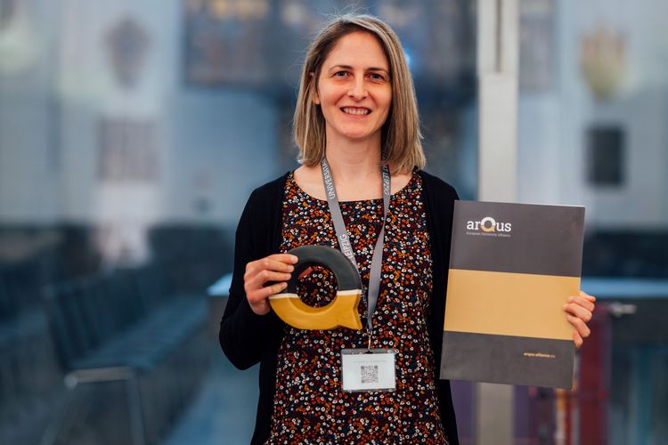 Silvia Kobe hält eine Urkunde und den Pokal, der aus einem schwarz-goldenen Buchstaben Q besteht, in die Kamera.