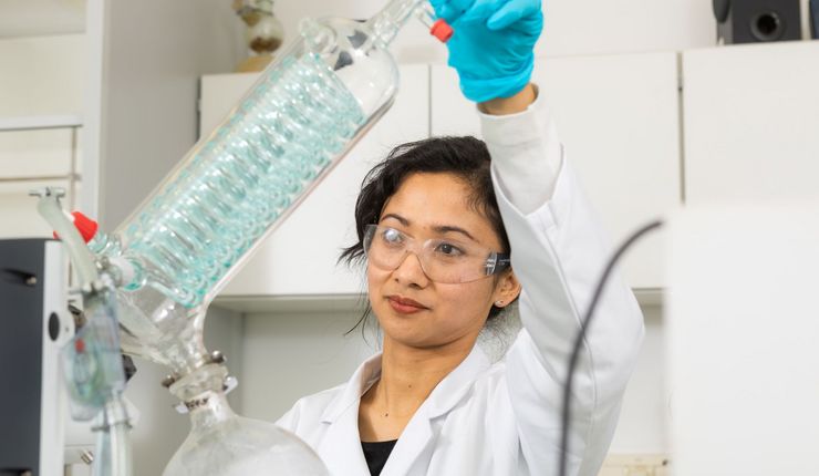 Eine Wissenschaftlerin steht in weißem Kittel in einem Labor und bedient ein analytischen Gerät