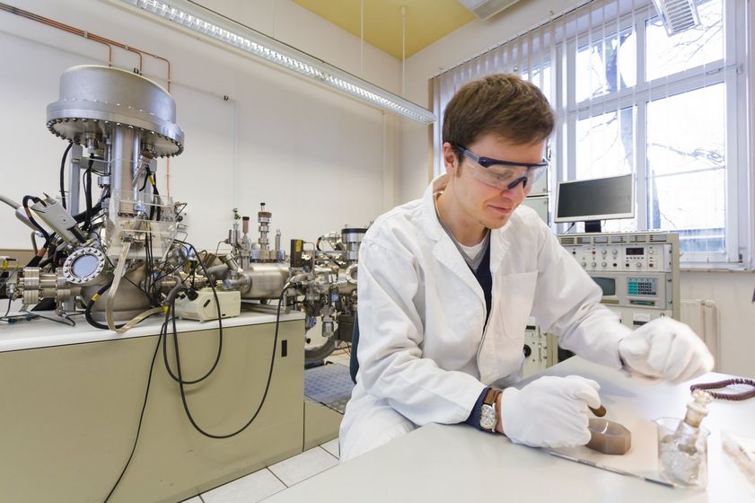 Student im weißen Kittel arbeitet im Labor mit einer Substanz. Er trägt Handschuhe und eine Schutzbrille, Foto: Christian Hüller
