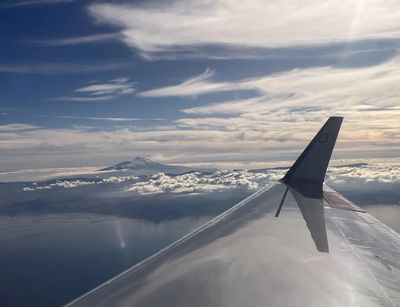 Ein Blick aus dem Flugzeug über den Wolken. Im Hintergrund ragt der Ätana heraus.