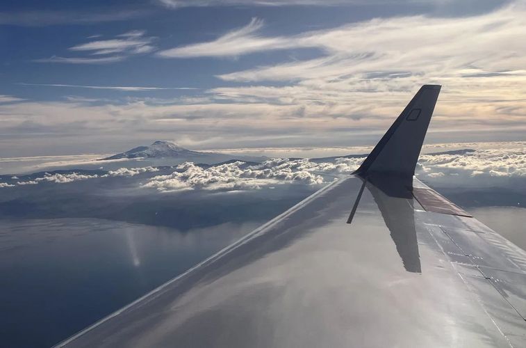 Ein Blick aus dem Flugzeug über den Wolken. Im Hintergrund ragt der Ätana heraus.