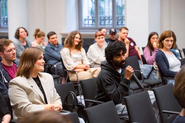 Mentee sitzt im Publikum und stellt eine Frage an die Referentin