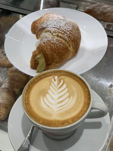 Farbfoto: Nahaufnahme einer Tasse Kaffee vor einem Croissant 