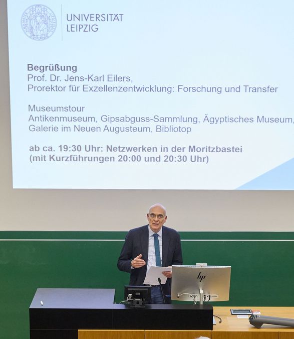 zur Vergrößerungsansicht des Bildes: Ein Mann steht im Hörsaal 8 vor den Gästen und begrüßt sie.