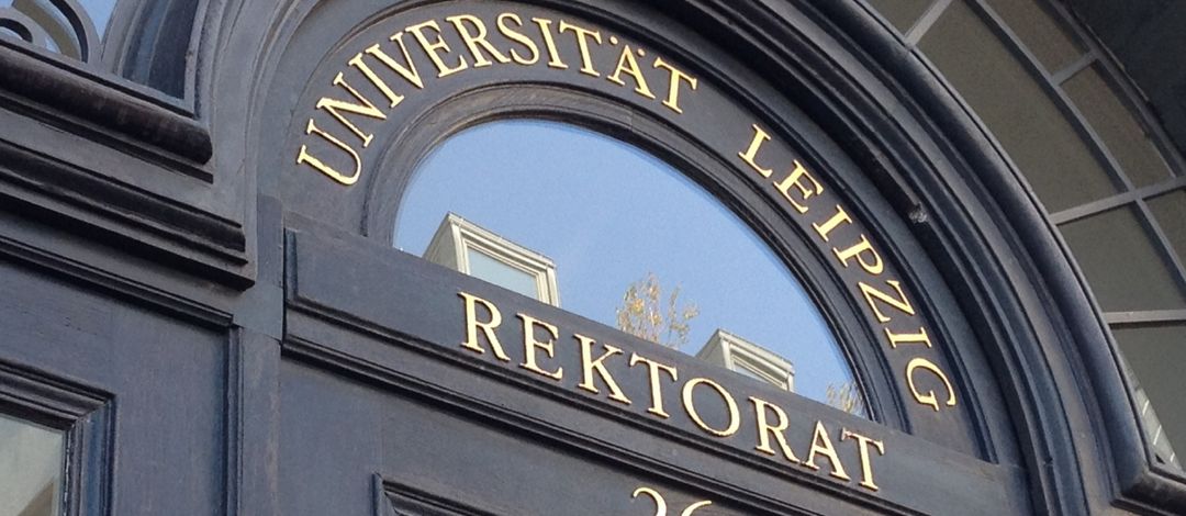 Farbfoto: Detailaufnahme der historischen Eingangstür zum Rektoratsgebäude in der Ritterstraße 26 aus dunklem Holz mit goldenem Schriftzug "Rektorat"
