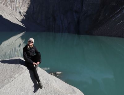 Person sitzt auf einem Stein, dahinter ein türkisfarbener See und hohe Felsen bei Sonnenschein