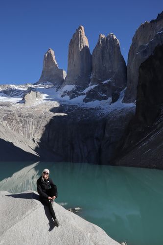 Person sitzt auf einem Stein, dahinter ein türkisfarbener See und hohe Felsen bei Sonnenschein