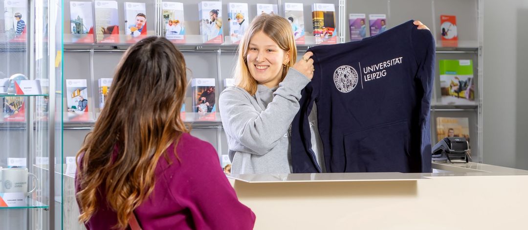 Junge Frau hält Pullover mit Universitätslogo hoch