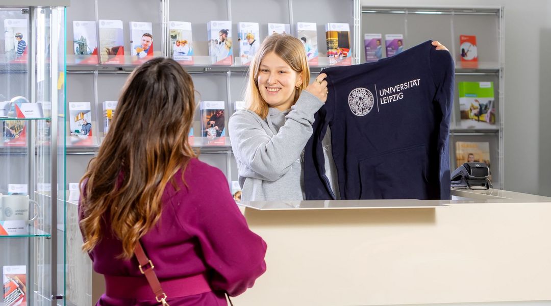 Junge Frau hält Pullover mit Universitätslogo hoch