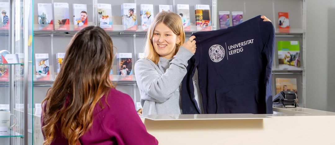 Junge Frau hält Pullover mit Universitätslogo hoch