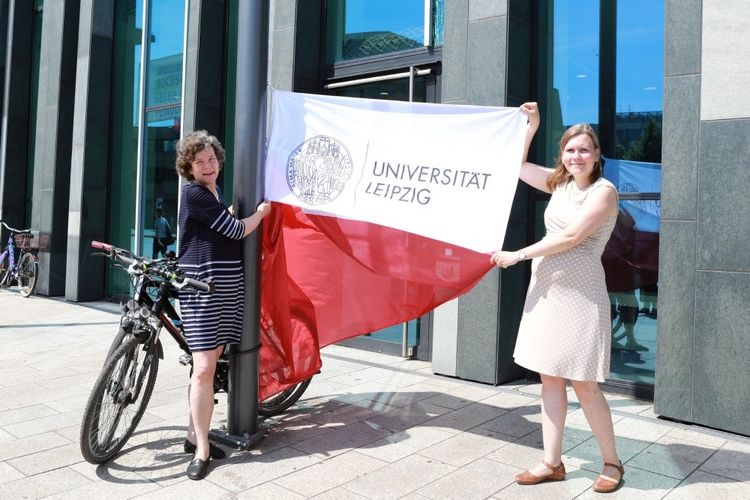 Rektorin Beate Schücking (links) und Madlen Mammen, Stabsstellenleiterin Universitätskommunikation, hissen vor dem Neuen Augusteum die Fahne mit dem neuen Logo.