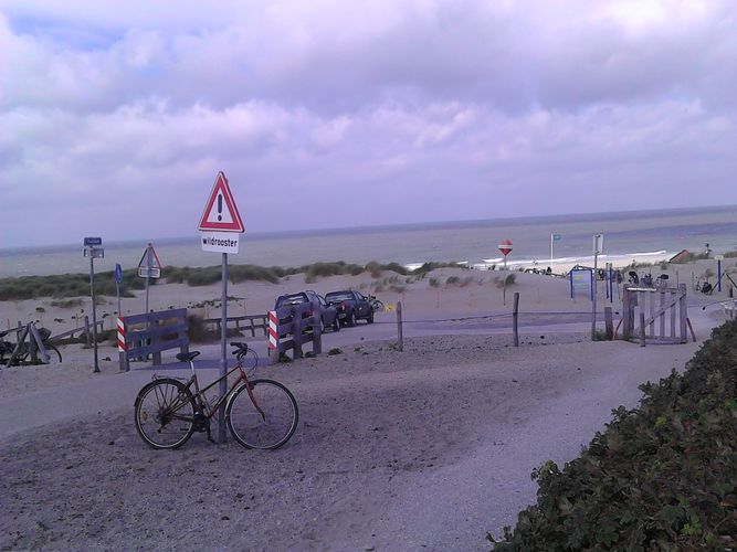 Hier sieht man den Blick auf einen Strand mit einem Fahrrad und einem Leuchtturm.