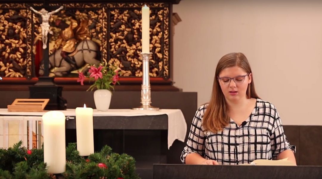 Eine Studentin liest aus der Bibel vor, vorne steht ein Adventskranz und im Hintergrund der Paulineraltar, Foto: Ole Depenbrock