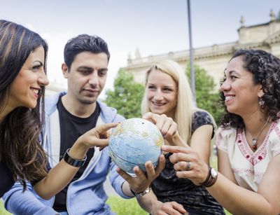 Internationale Studierende zeigen auf eine Erdkugel