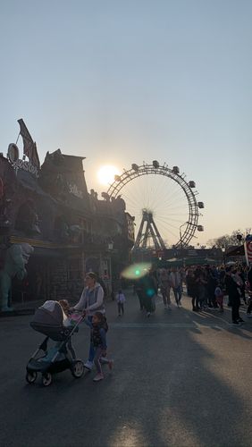 Ein Riesenrad ist in der hinteren Bildmitte zu sehen. Davor sieht man eine Kirmes mit Buden.