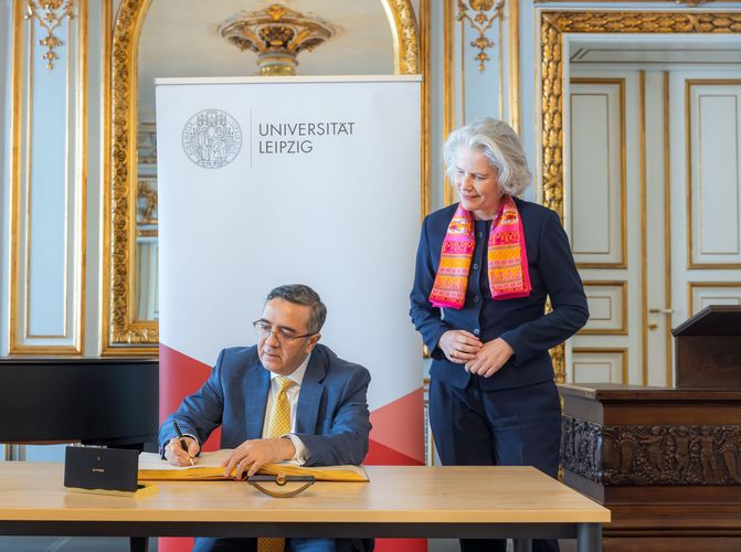 Zu sehen ist sitzend und ins Goldene Buch der Uni Leipzig schreibend der Botschafter Indiens in Deutschland, Ajit Vinayak Gupte. Neben ihm steht Rektorin Prof. Dr. Eva Inés Obergfell. Foto: Swen Reichhold