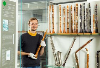 Zu sehen ist Fabian Everding vor einer Vitrine, in der zahlreiche historische Klarintten zu sehen sind.