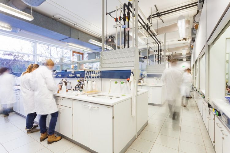Innenansicht eines Labors, in dem Personen in weißen Kitteln mit unterschiedlichen Substanzen arbeiten, Foto: Christian Hüller