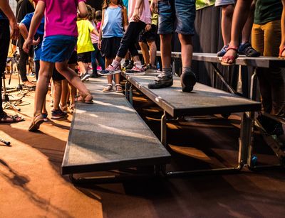 Auf dem Bild sind die Beine von Kindern, die gemeinsam auf einer Bühne stehen, zu sehen.