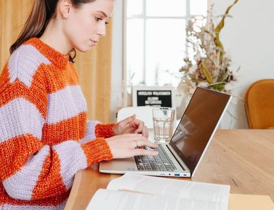 Junge Frau sitzt am Schreibtisch, vor ihr steht ein aufgeklappter Laptop, Foto: Grit Hartung