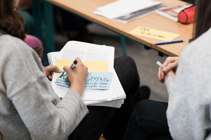 Man sieht zwei Studentinnen von hinten auf Stühlen sitzend. Sie schreiben gerade etwas auf Karteikarten, Foto: Christian Hüller