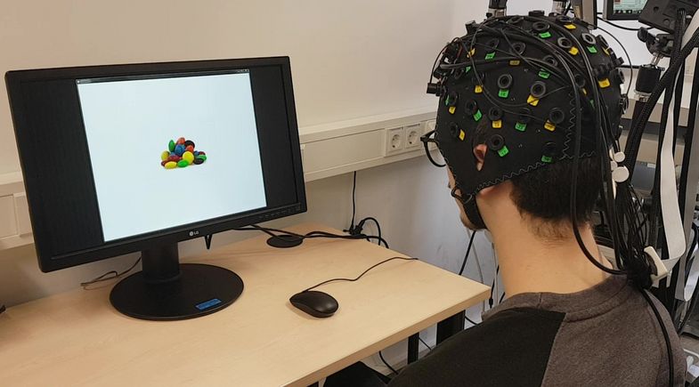 Aufbau des fNIRS-Neurofeedback: Auf dem Monitor sehen die Teilnehmenden Bilder von Nahrungsmitteln, die während eigener Essanfälle gegessen wurden. Ziel ist es, die Nahrungsbilder zu verkleinern, indem die Hirnaktivität in individuell bestimmten Hirnarealen des präfrontalen Kortex erhöht wird, um die kognitive Kontrolle in Bezug auf die dargestellten Nahrungsmittel zu erhöhen und somit Essanfälle zu reduzieren.