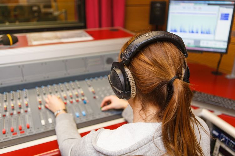 Studentin mit Kopfhörern sitzt vor einem Mischpult im Hörstudio, Foto: Christian Hüller 