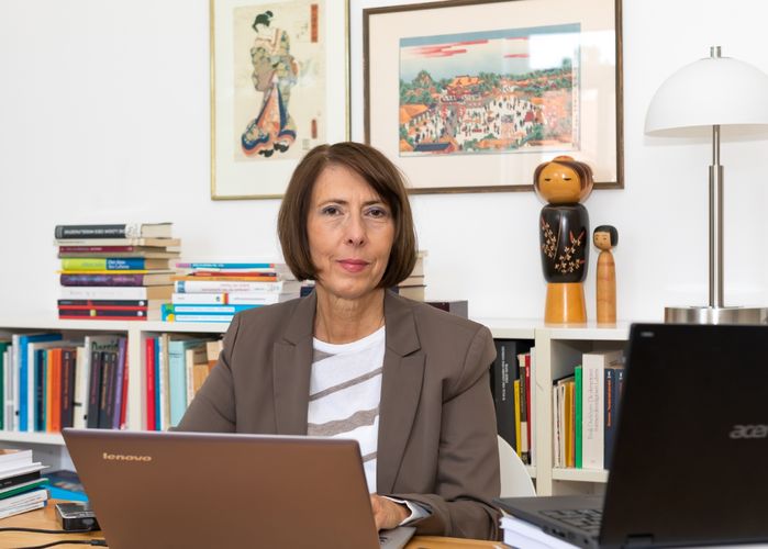 Professorin Barbara Drinck sitzt an ihrem Schreibtisch in einem hellen Arbeitszimmer. Vor ihr steht ein aufgeklappter Laptop. Sie blickt in die Kamera.