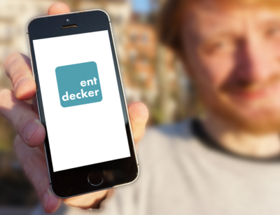 Mann hält lächelnd ein Smartphone in die Kamera, wo das Logo der Entdecker-App angezeigt wird, Foto: Martha Fromme, Universität Leipzig