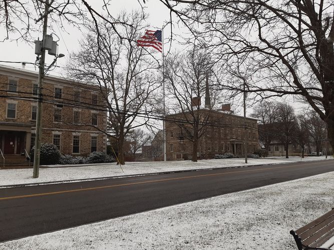 Eine Straße mit prachtvollen Häusern. Es schneit. Zwischen zwei Häusern weht eine US-amerikanische Flagge.