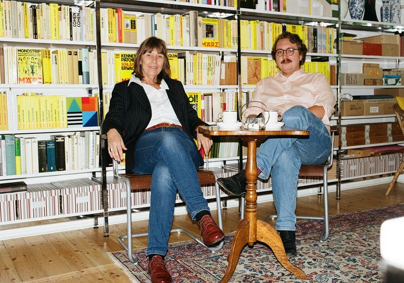 Eine Frau und ein Mann sitzen an einem Stehtisch vor einem Bücherregal