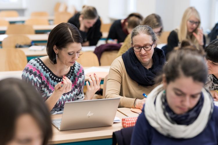 Zwei Studentinnen sind fokussiert, die zusammen mit anderen im Seminarraum sitzen. Sie scheinen über etwas zu reden und wirken ratlos, Foto: Christian Hüller 