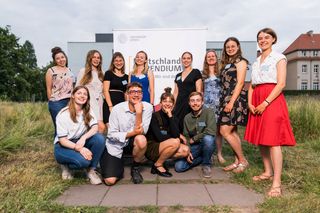 Stipendiatinnen und Stipendiaten des Deutschlandstipendiums stehen auf einer Wiese in der Veterinärmedizinischen Fakultät vor dem Rollup des Deutschlandstipendiums