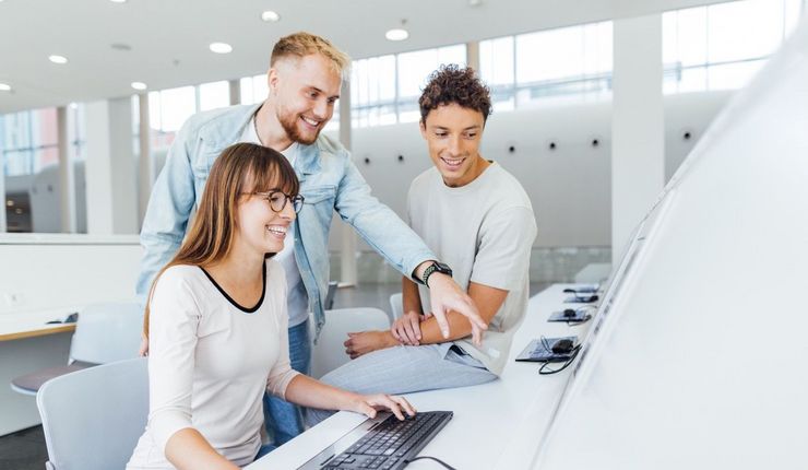 Drei Studierende vor einem PC-Arbeitsplatz im Foyer des Neuen Augusteums der Uni Leipzig