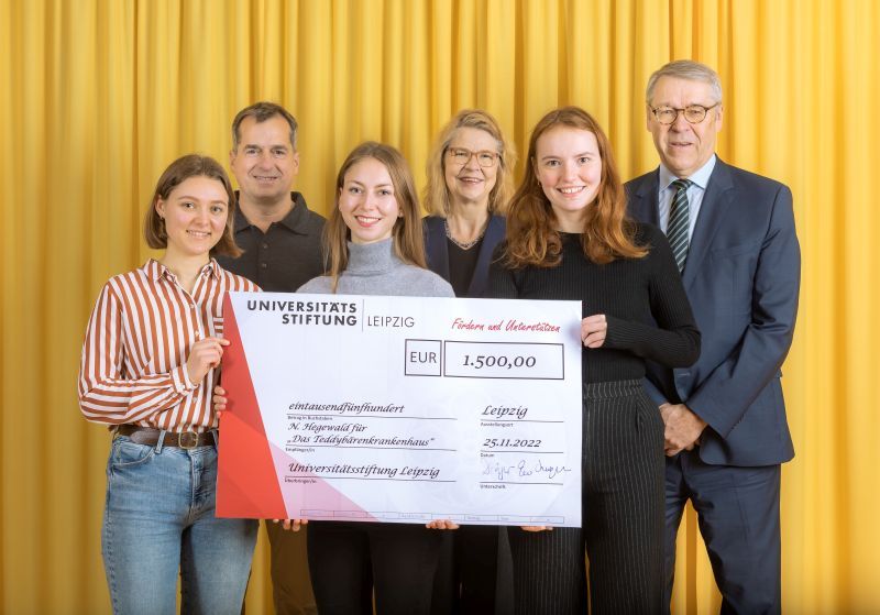 zur Vergrößerungsansicht des Bildes: Farbfoto: Prof. Dr. Birgit Dräger, Dr. Hubert Temmeyer und Prof. Dr. Harald Krautscheid von der Universitätsstiftung überreichen den symbolischen Scheck an die Fördermittelempfängerinnen Nora Hegewald, Elisabeth Krieger und Sina Fischer