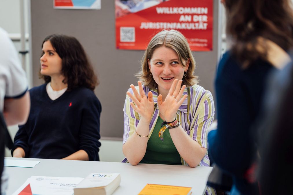 zur Vergrößerungsansicht des Bildes: Foto: Studentin, die am Stand der Juristenfakultät mit Besucher:innen spricht.