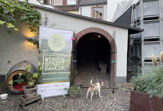 Eingang des Weinguts Breuer mit einem Banner zum Heimspiel Wissenschaft, davor ein Hund
