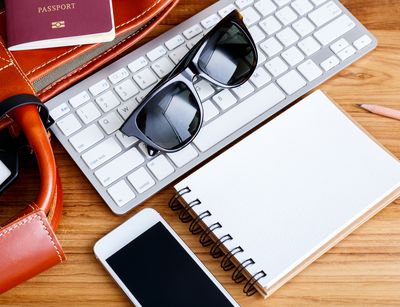 Tastatur, Sonnenbrille, Notizbuch, Smartphone, Reisetasche und Reisepass liegen nebeneinander auf einem Tisch