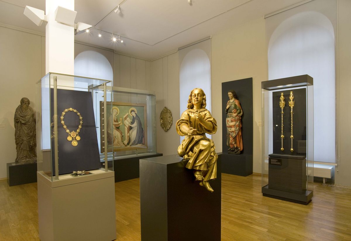 zur Vergrößerungsansicht des Bildes: Foto: Ausstellungsstücke aus der Kustodie werden gezeigt, im Vordergrund eine goldene Statue, im Hintergrund weitere religiöse Statuen und Malereien.