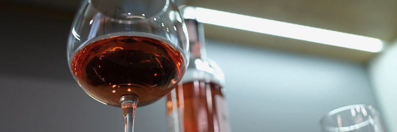 Detailaufnahme: aus der Froschperspektive ist ein gefülltes Weinglas zu sehen, dahinter steht eine Weinflasche und am oberen Rand ist noch eine Bürolampe zu erkennen.