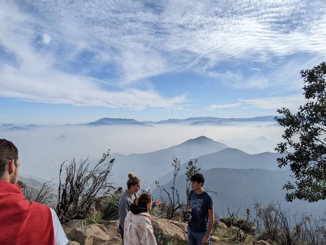 Personen stehen auf Berg und blicken auf das vernebelte Gebirge unter ihnen bei Tag