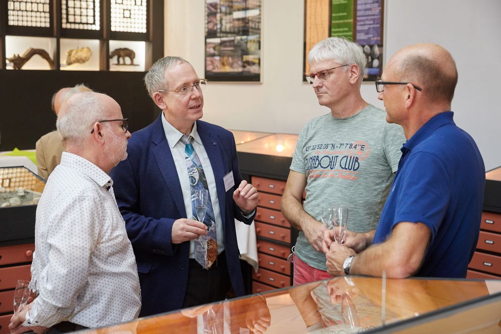 Farbfoto: Prorektor Professor Gläser spricht mit drei älteren Herren im Ausstellungsraum.