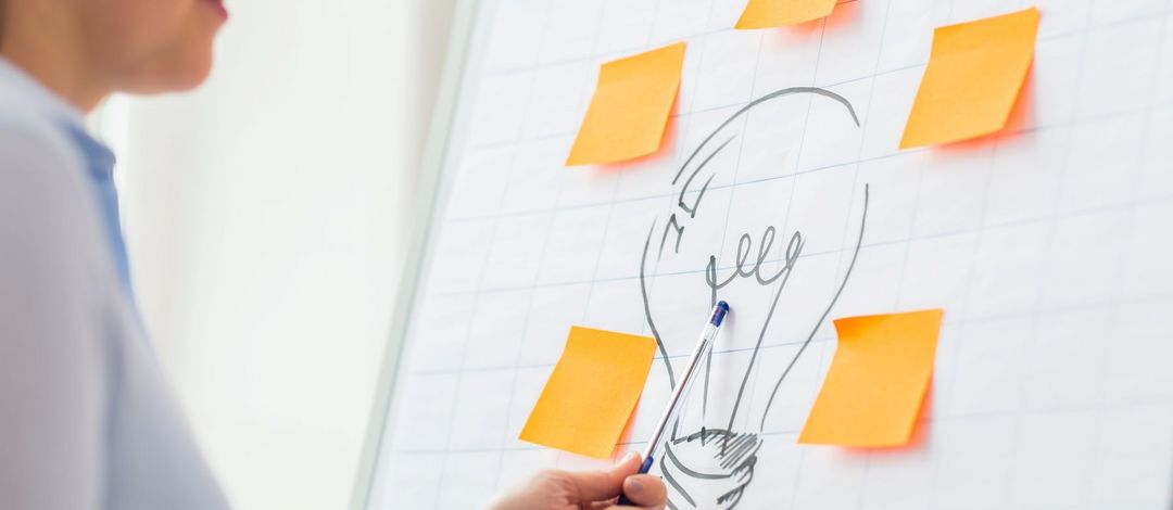 Farbfoto: Das Foto zeigt ein Flipchart, auf das eine Glühbirne aufgemalt ist. Daneben kleben farbige Post-Its.