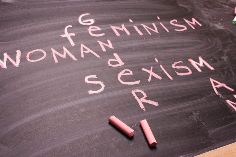 Farbfoto: Detailaufnahme einer Schultafel, auf der mit rosafarbender Kreide die Worte "Gender", "Feminismus", "Woman" und "Sexismus" geschrieben sind.