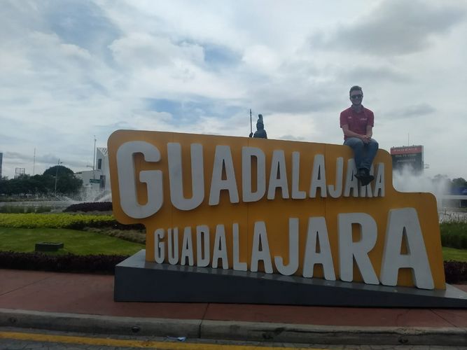 Karl sitzt auf einem großen orangenen Schild, auf welchem zwei Mal untereinander "Guadalajara" in weiß steht.