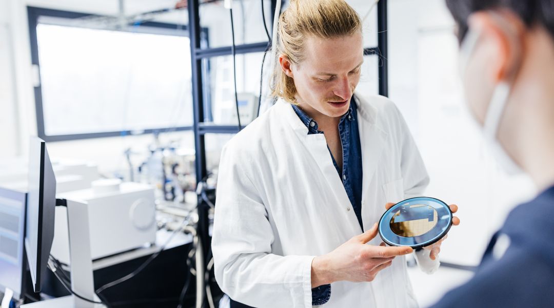 Doctoral researcher showing gold wafer targets (Photo: Christian Hüller / Leipzig University, RTG 2721)