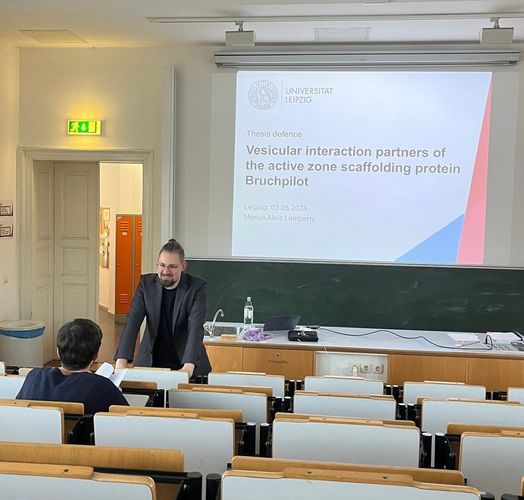 A man standing in front of the lecture hall with the projector wall behind him